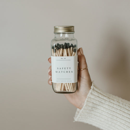 Hand holding a glass jar of safety matches with a plain background