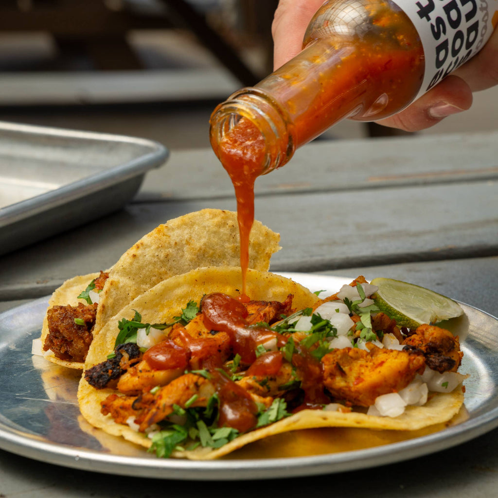 Person pouring hot sauce onto tacos with a bottle labeled 'Bolt'.